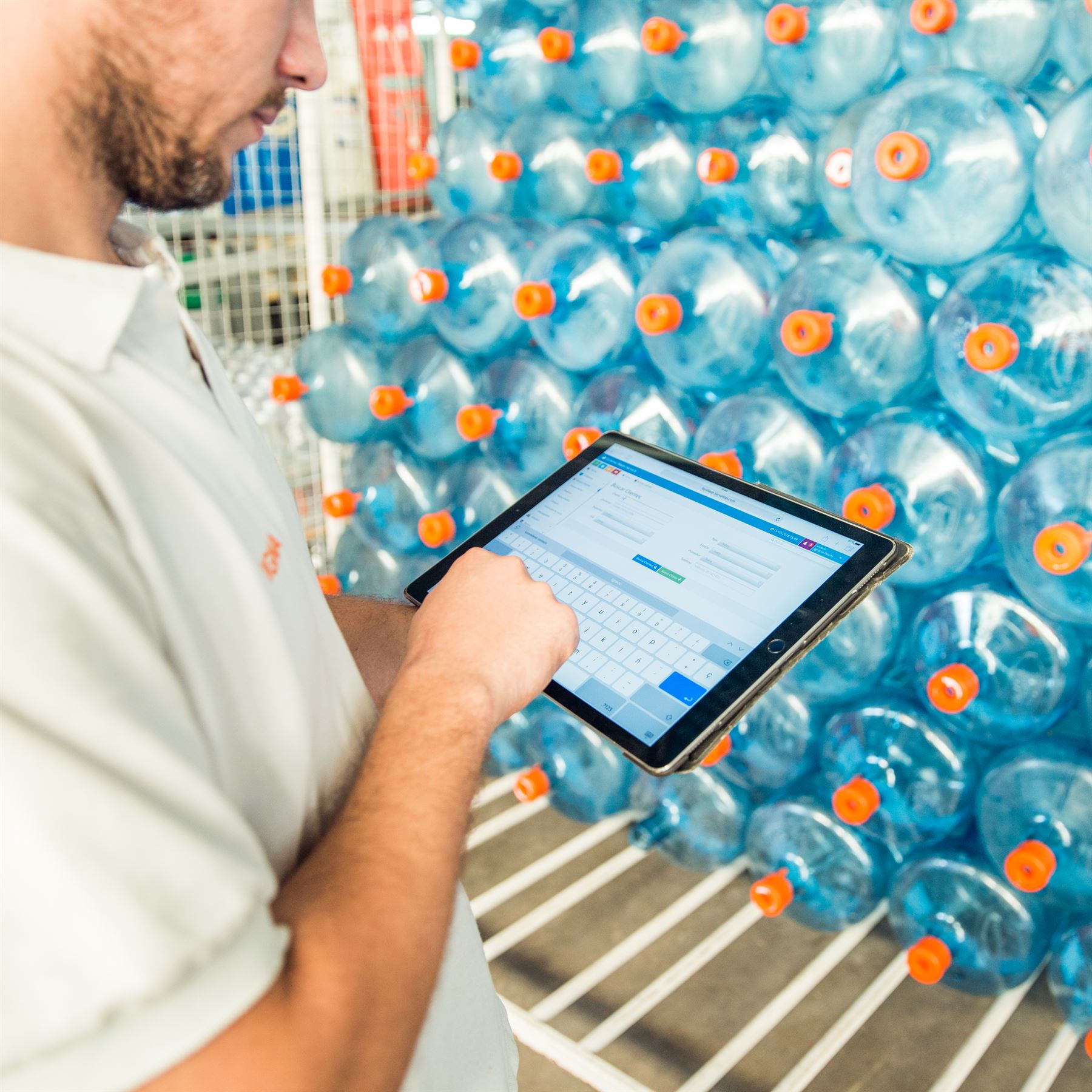 Repartidor consultando la ficha de un cliente en una tablet, frente a un pallet de bidones